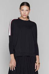 Woman wearing a black sweater with white and red stripes on a gray background