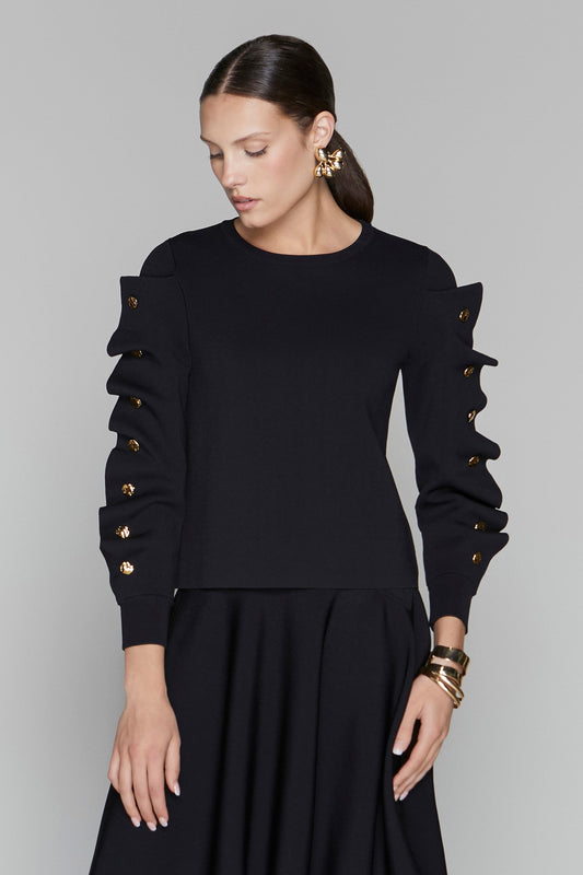 Woman wearing a black outfit with gold buttons on a gray background