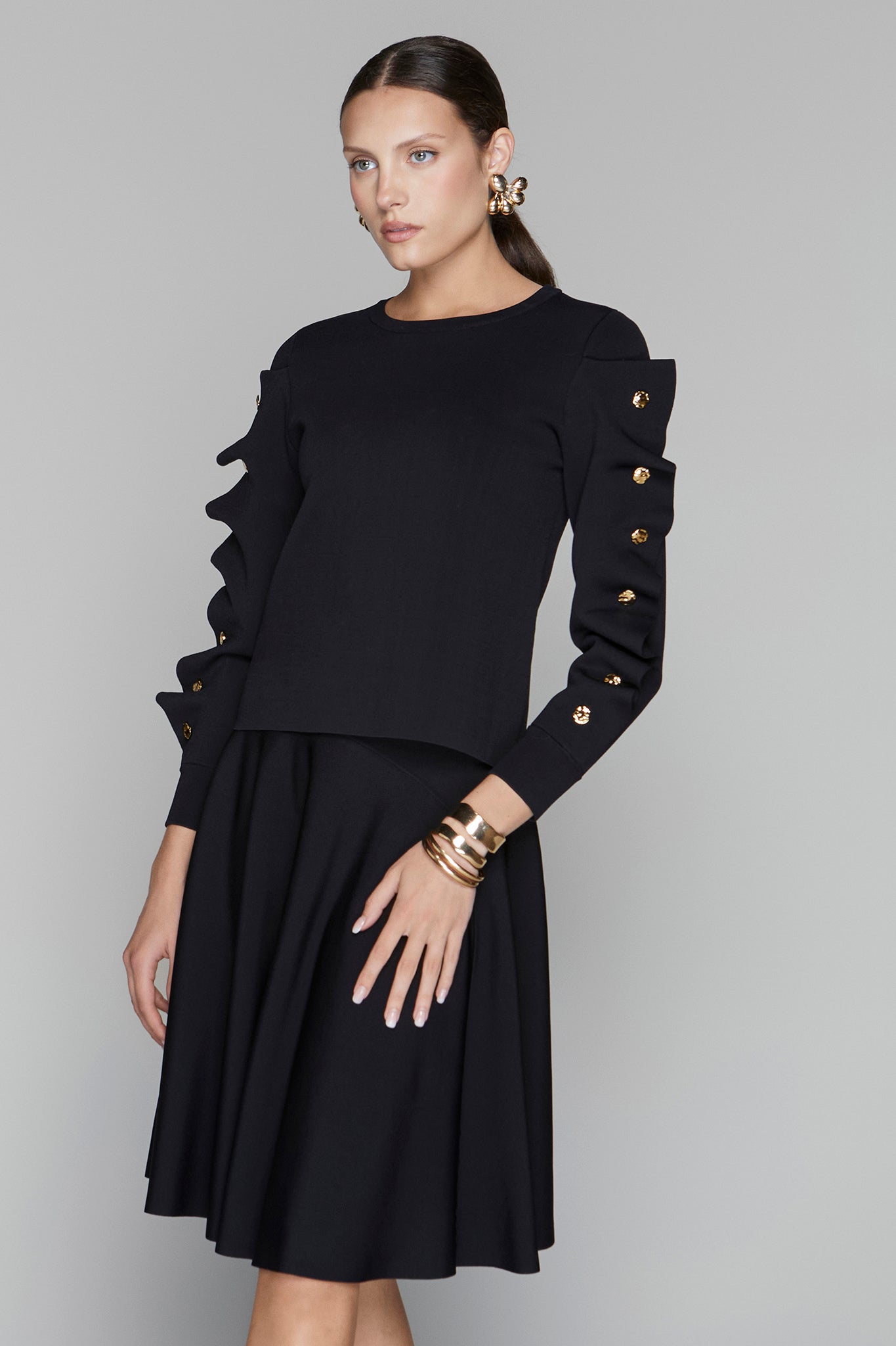 Woman wearing a black dress with gold buttons on a gray background
