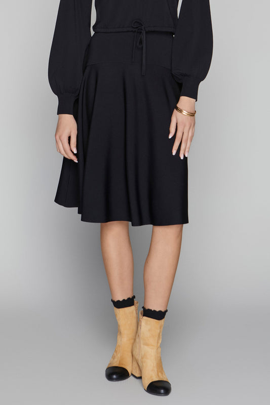 Person wearing a black dress with beige shoes on a gray background