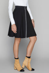 Person wearing a black skirt with a zipper, white long-sleeve top, and beige boots on a gray background