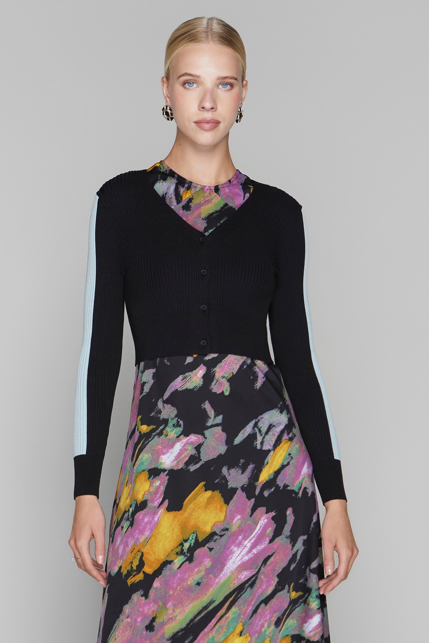 Woman wearing a black cardigan over a colorful dress with a gray background