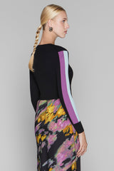 Woman wearing a black sweater with colorful side panels and a floral skirt on a gray background