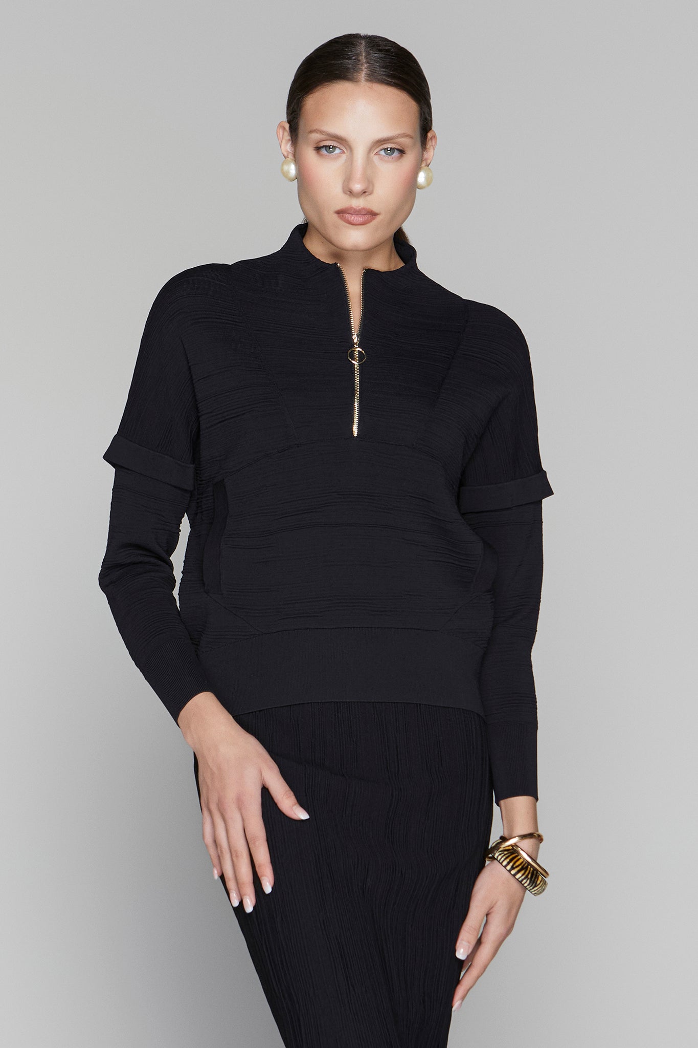 Woman wearing a black outfit with a quarter zip on a gray background