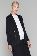 Woman wearing a black blazer with gold buttons and a white shirt on a gray background