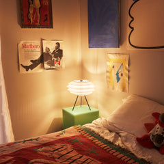 Room interior with a lamp, posters, and a bed with a colorful blanket.
