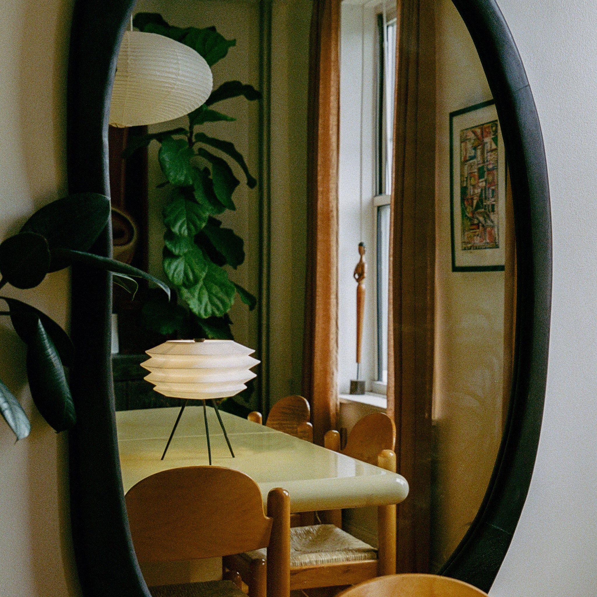Dining room with round mirror reflecting a table and chairs, plant, and window.
