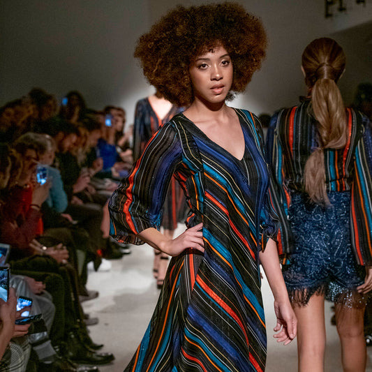 Model walking on a fashion show runway wearing a colorful striped dress.