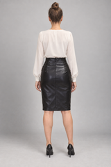 A woman shown from the back wearing a cream-colored long-sleeve blouse and a black faux-leather pencil skirt, paired with black heels, against a neutral gray studio background.