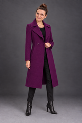 A woman modeling a long, double-breasted purple wool coat over a black outfit, standing against a dark gray studio background.