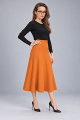A woman modeling a black long-sleeve top and a high-waisted, pleated orange A-line midi skirt, paired with black pointed-toe heels, against a solid gray studio background.