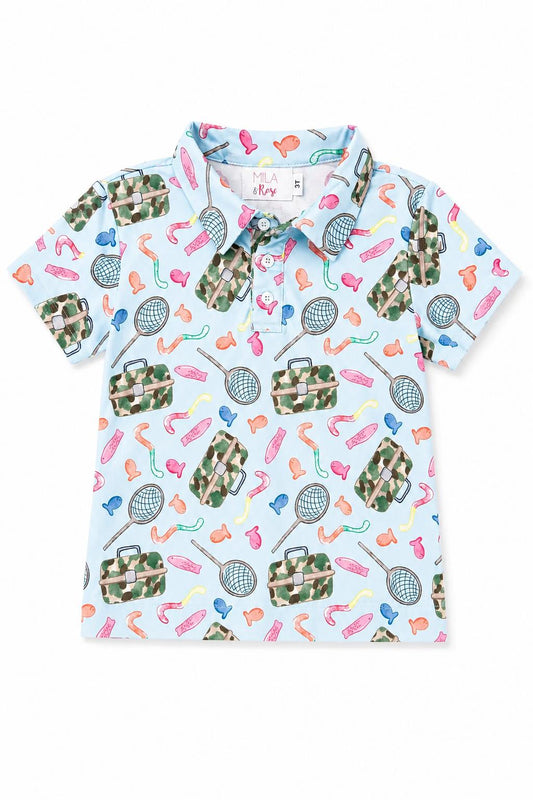 A short-sleeve polo shirt for kids on a white background, featuring a light blue base with a colorful pattern of tennis rackets, bags, and athletic shoes in green camouflage and bright colors.