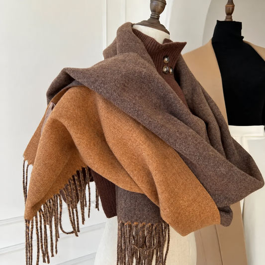 A large woven shawl scarf in two shades of brown draped over a dress form, with fringe trim hanging from the corners. The shawl is shown on a mannequin in an indoor studio setting.