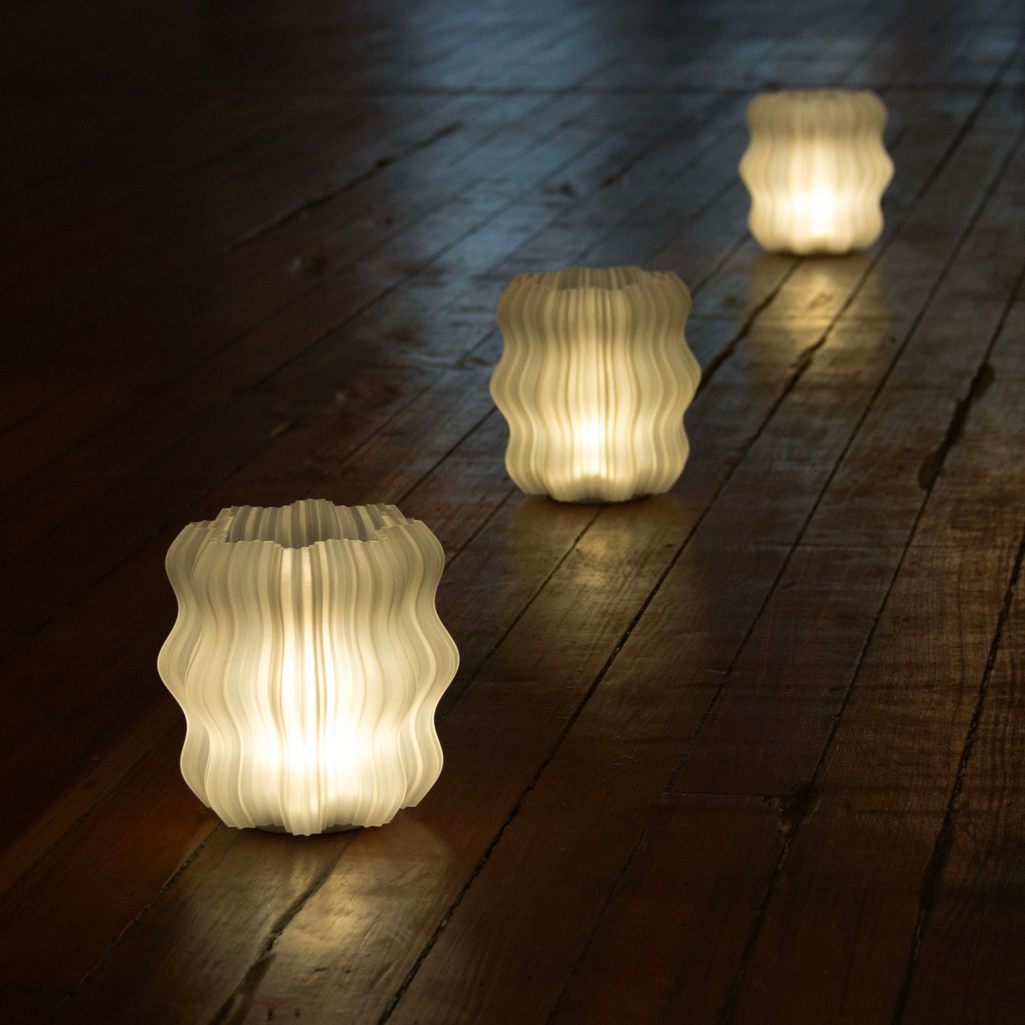 Three illuminated glass lanterns on a wooden surface