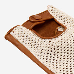 Close-up of a brown leather driving glove with cream crochet detailing on a white background