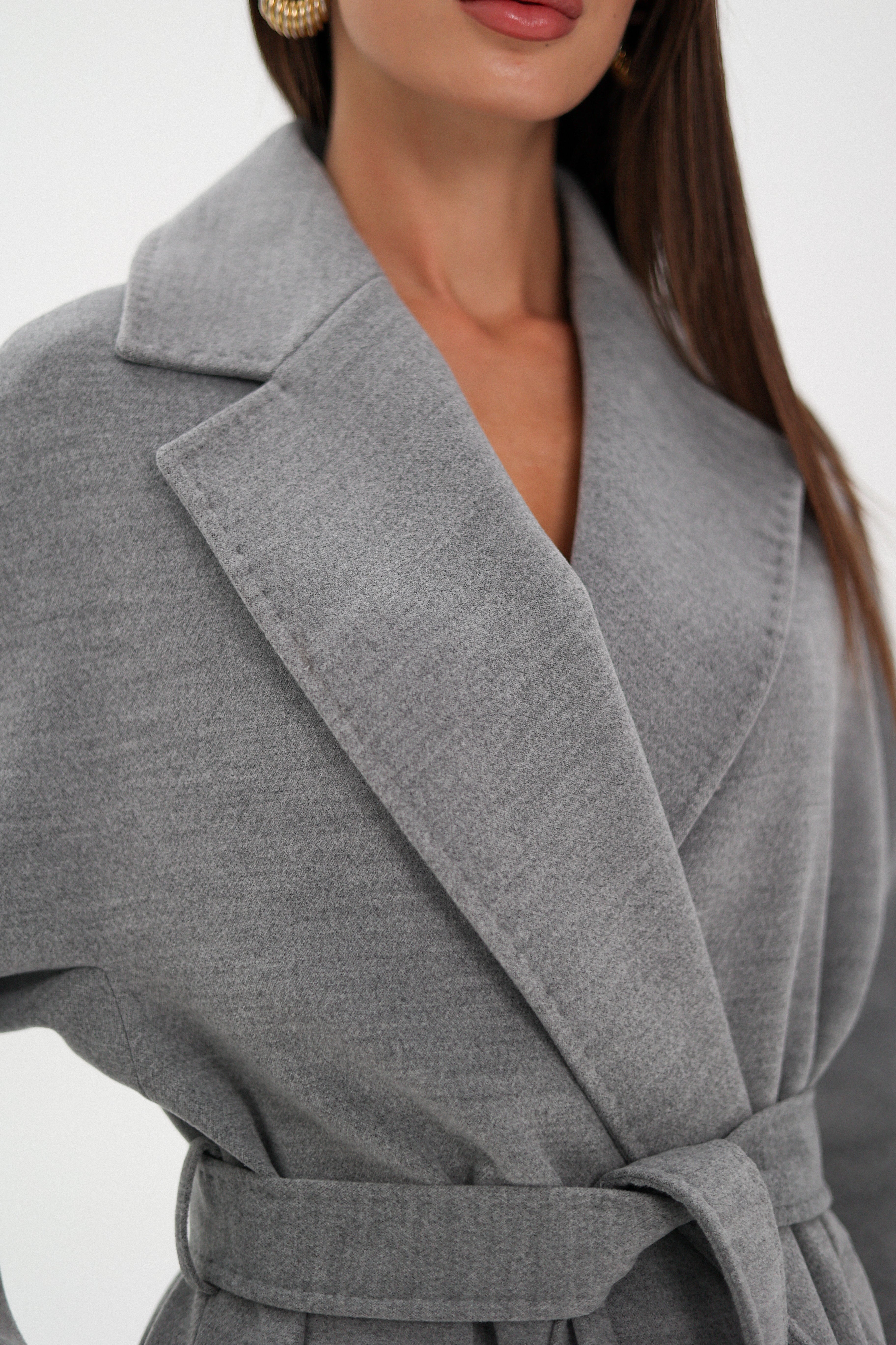 Woman wearing a gray coat over a black outfit on a white background