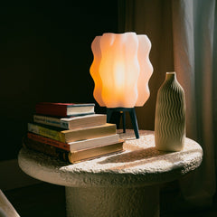 Futuristic lamp with wavy design on a table with books and a vase.