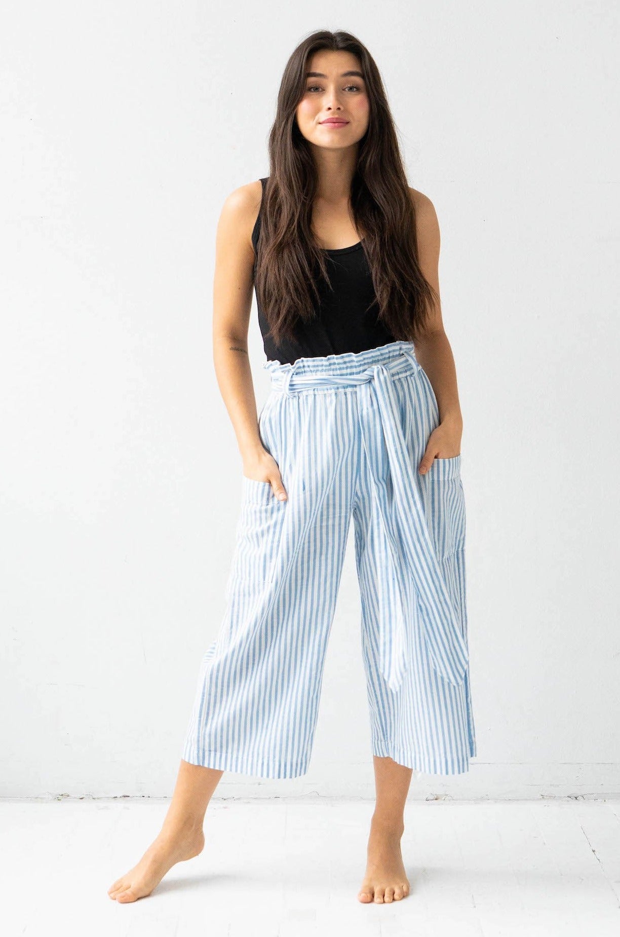 Woman wearing light blue striped pants and a black top on a white background