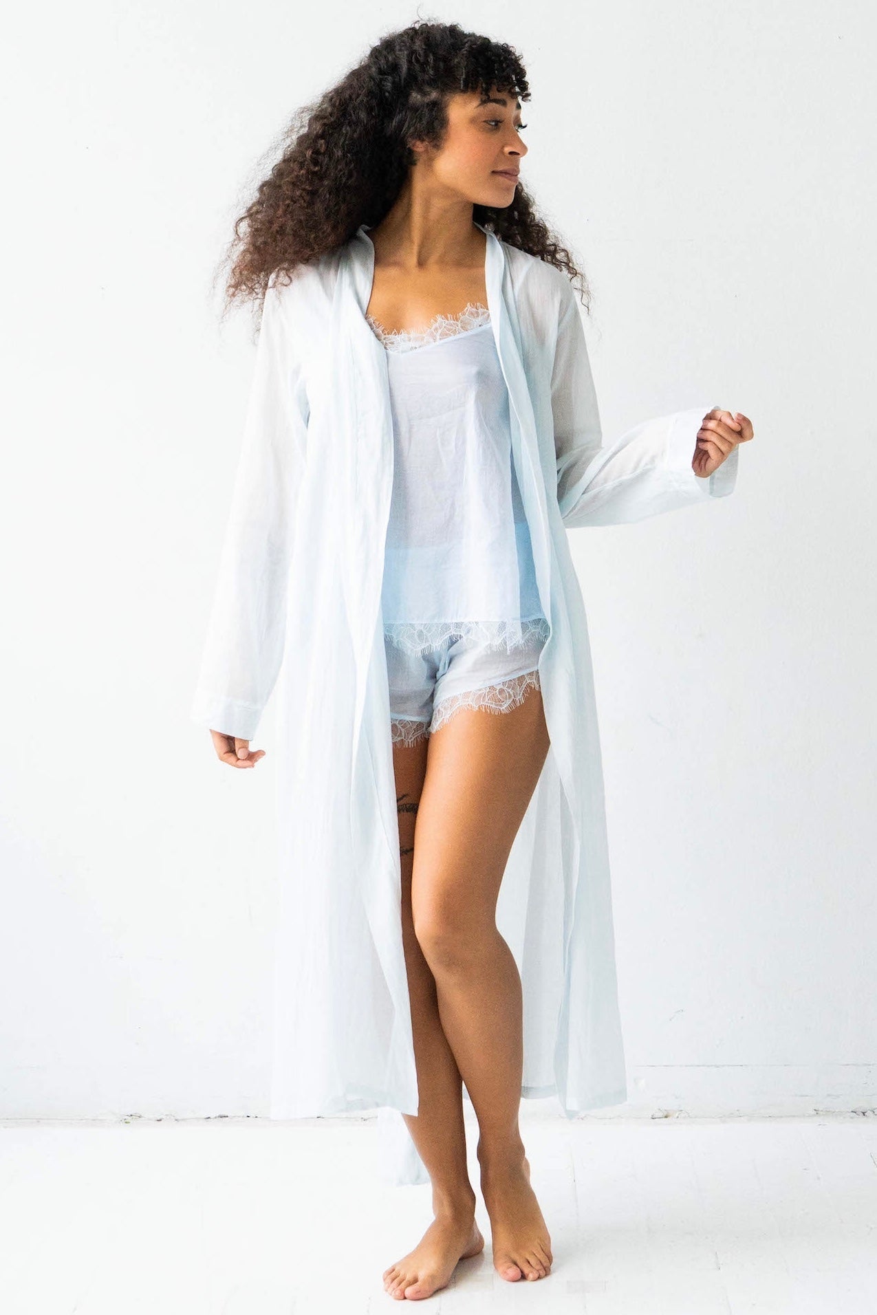 Woman wearing a sheer white robe over a light blue nightgown on a white background