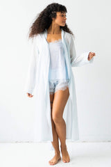 Woman wearing a sheer white robe over a light blue nightgown on a white background