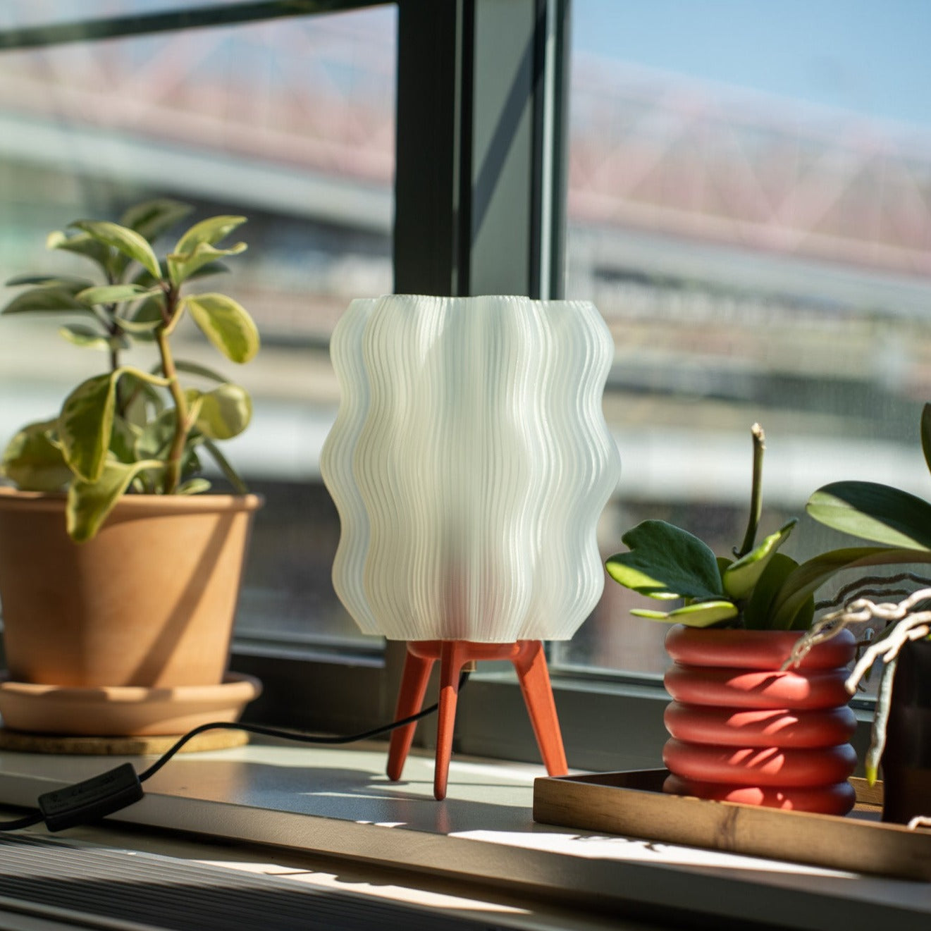 White textured lamp on a windowsill with plants and a blurred outdoor view