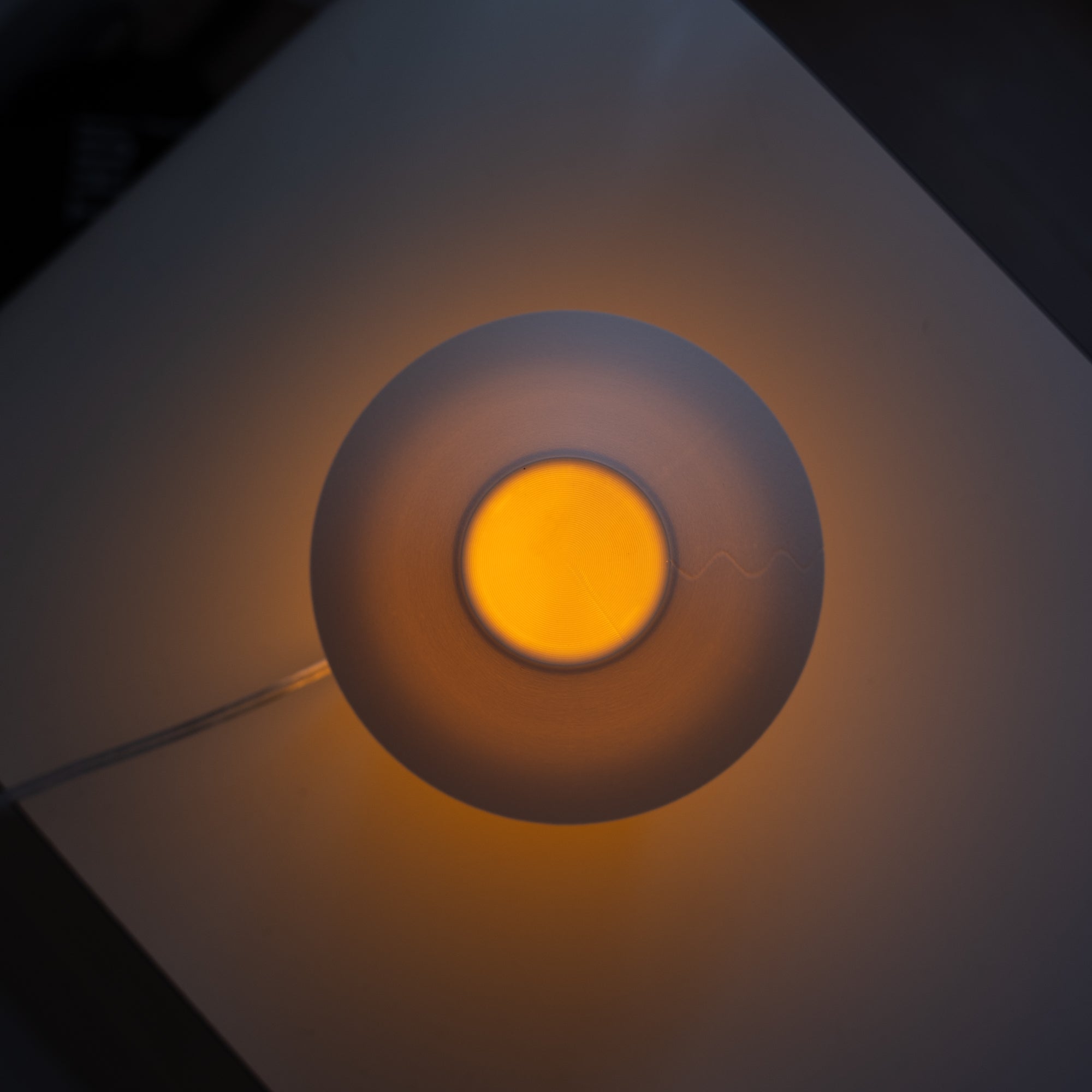 Round light fixture with a glowing yellow center on a dark background
