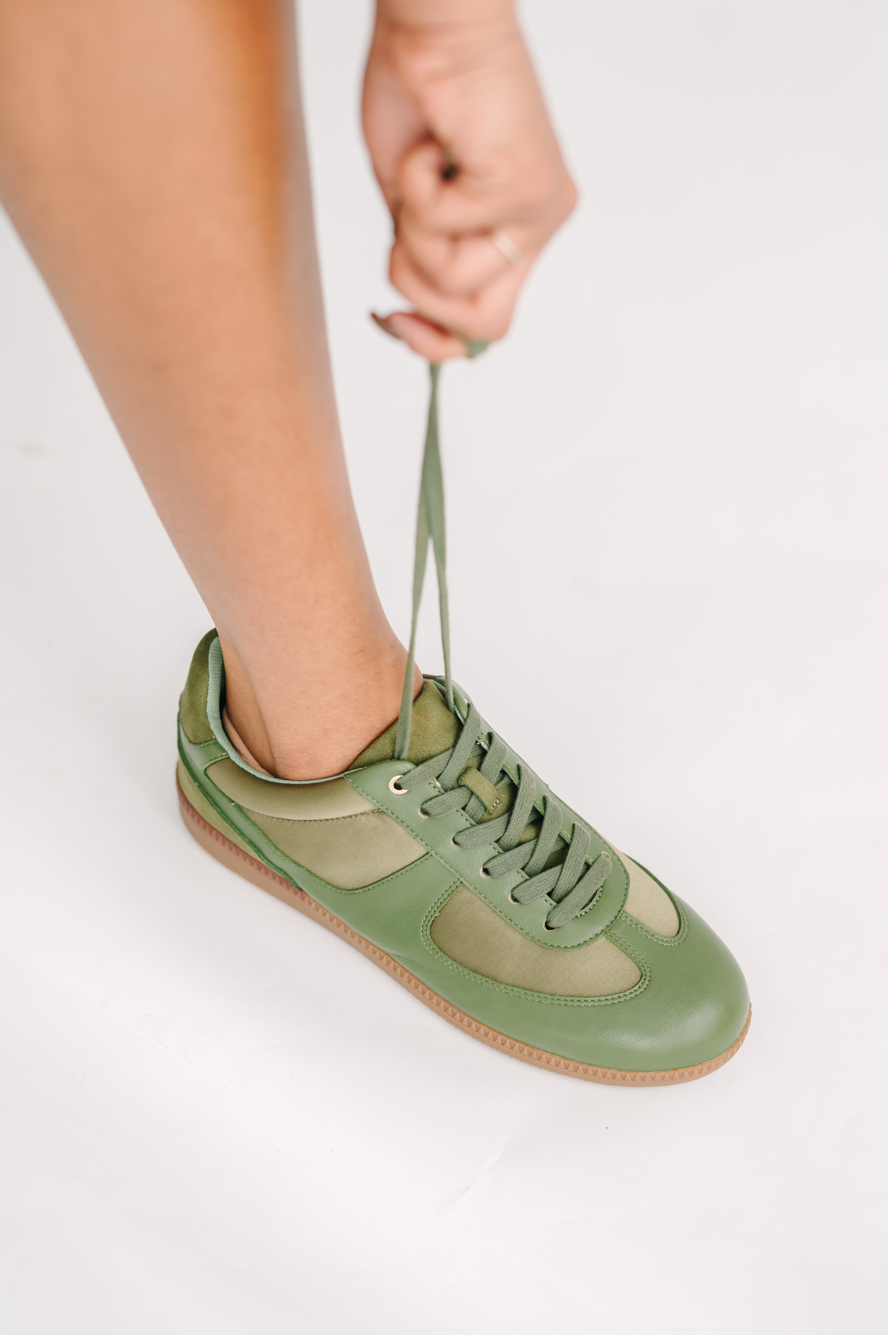 Green sneaker being tied on a white background