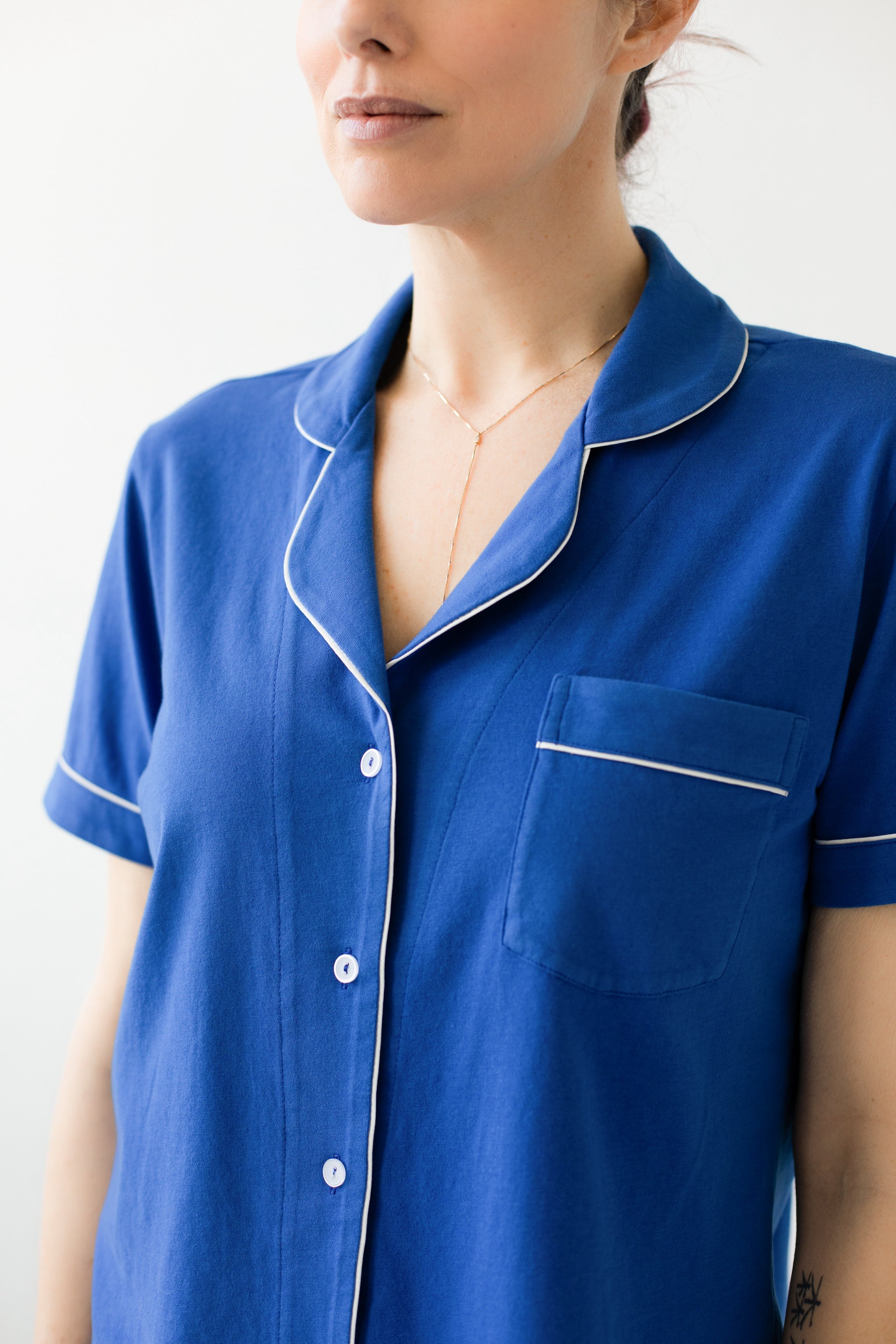 Person wearing a blue pajama top with white trim on a plain background