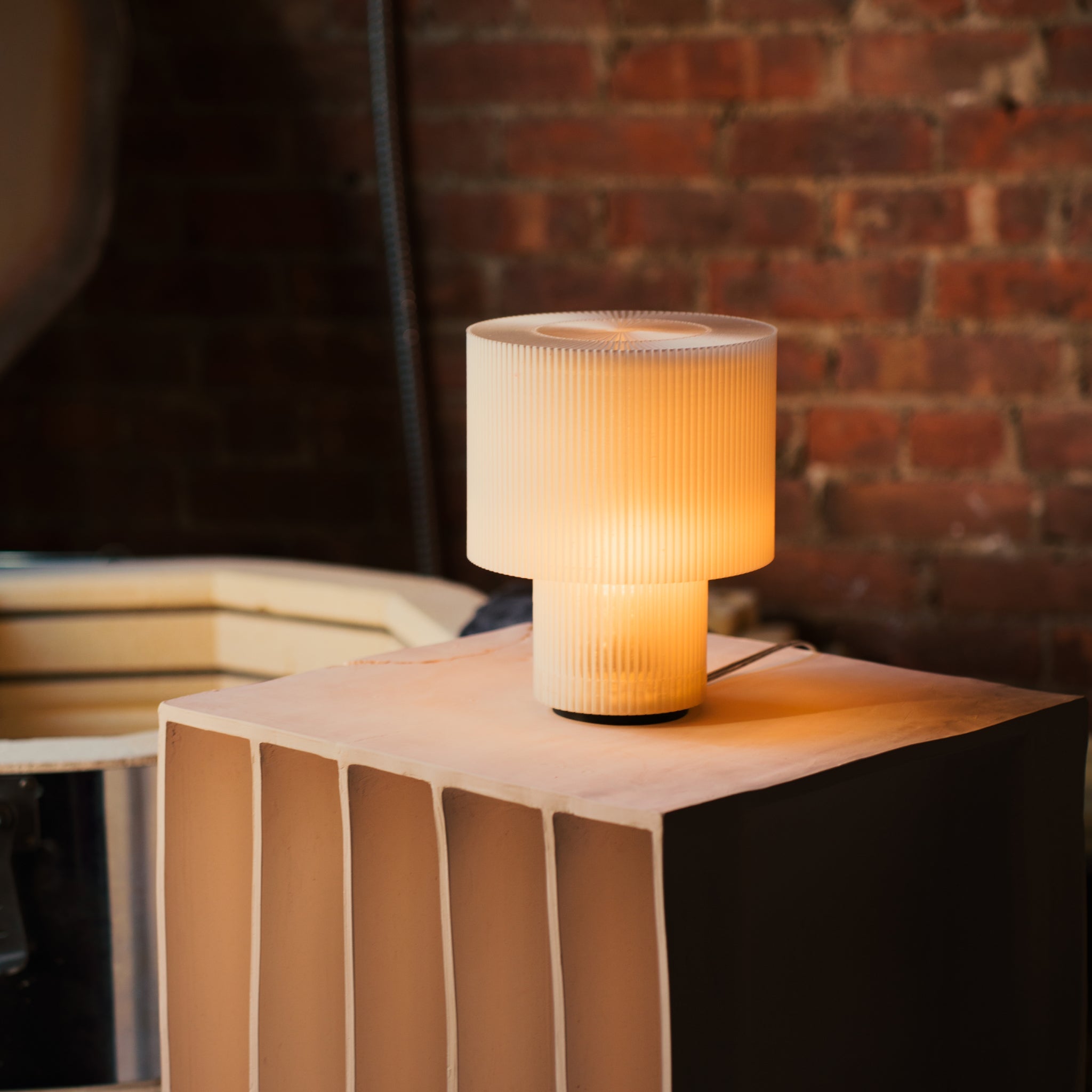 Table lamp with ribbed design on a wooden surface against a brick wall.
