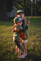 Two children hugging in a grassy field with a sunset or sunrise light.