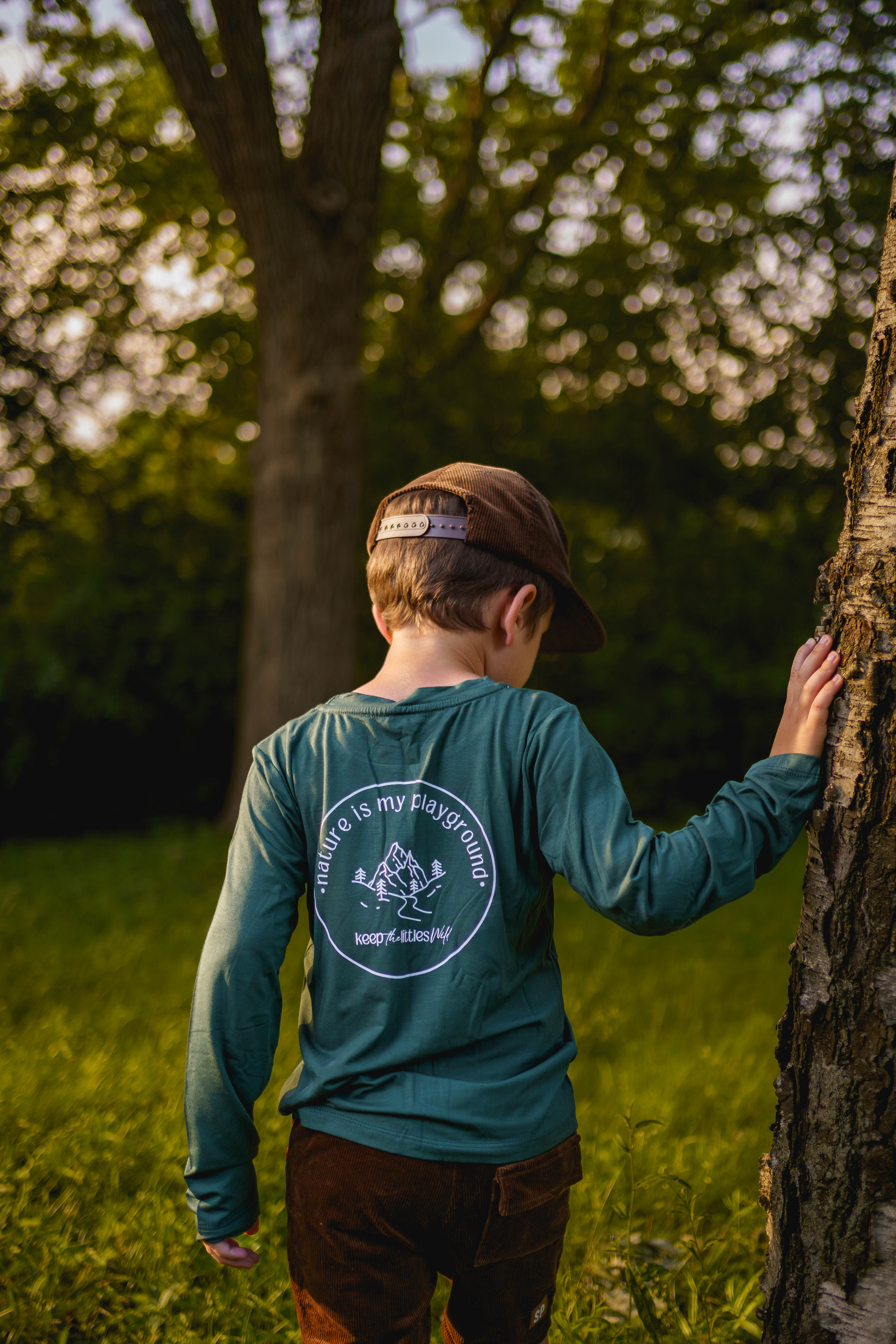 Child wearing a green shirt with a logo, standing in a natural setting.