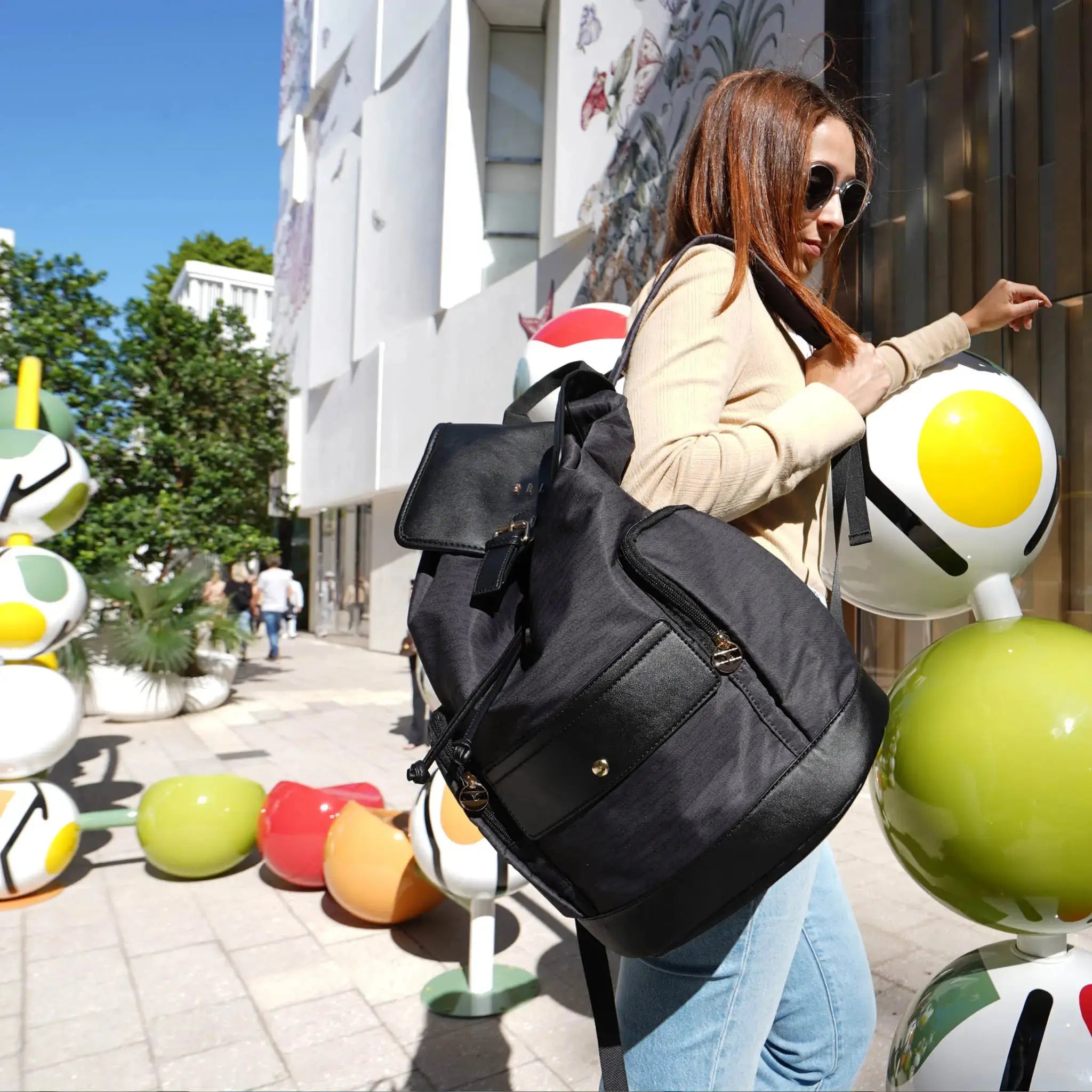 Woman with a black backpack walking on a street with colorful sculptures.