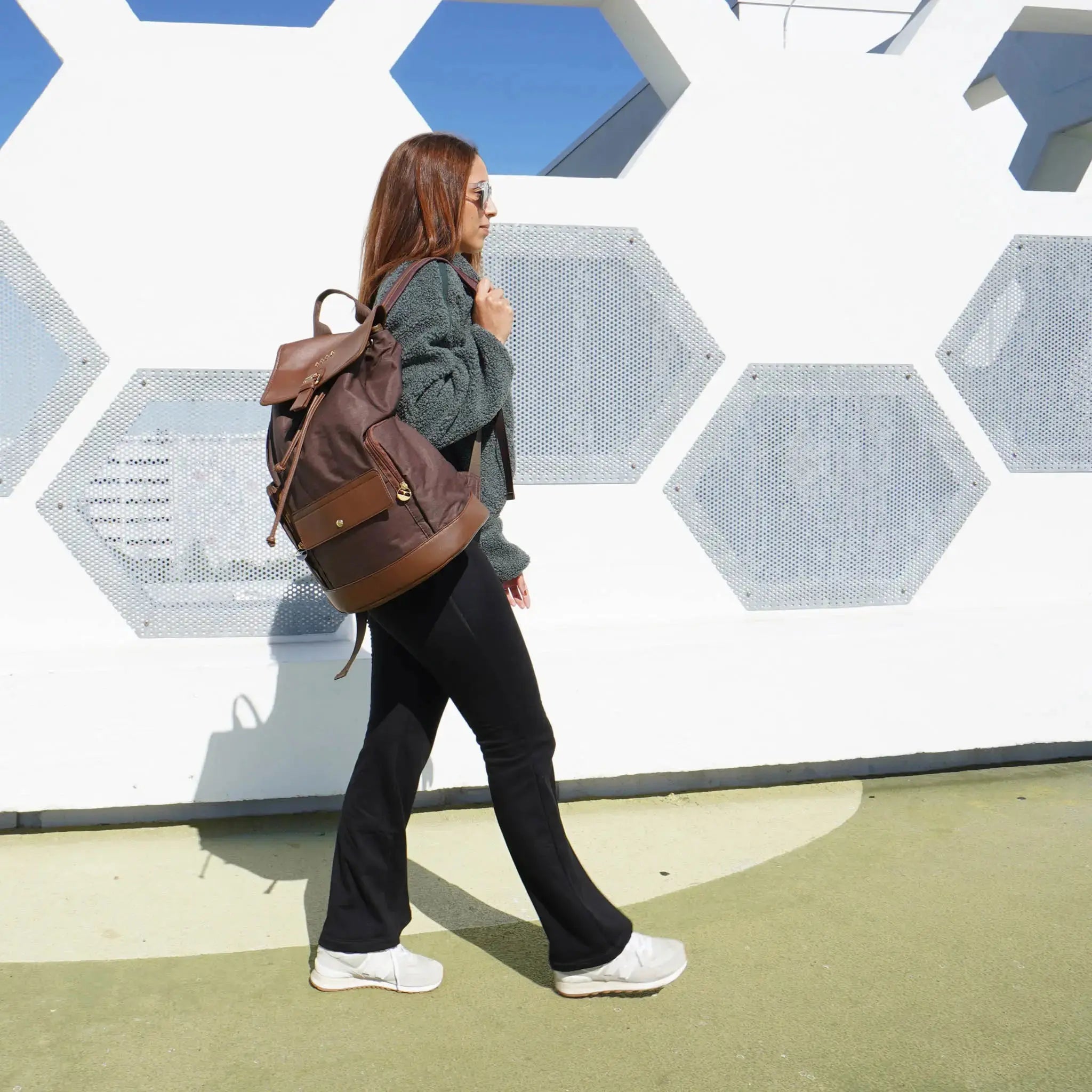 Person with a brown backpack walking past a geometric-patterned wall.