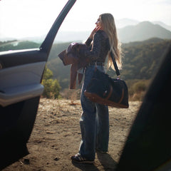 Woman with a bag standing next to an open car door in a scenic outdoor setting