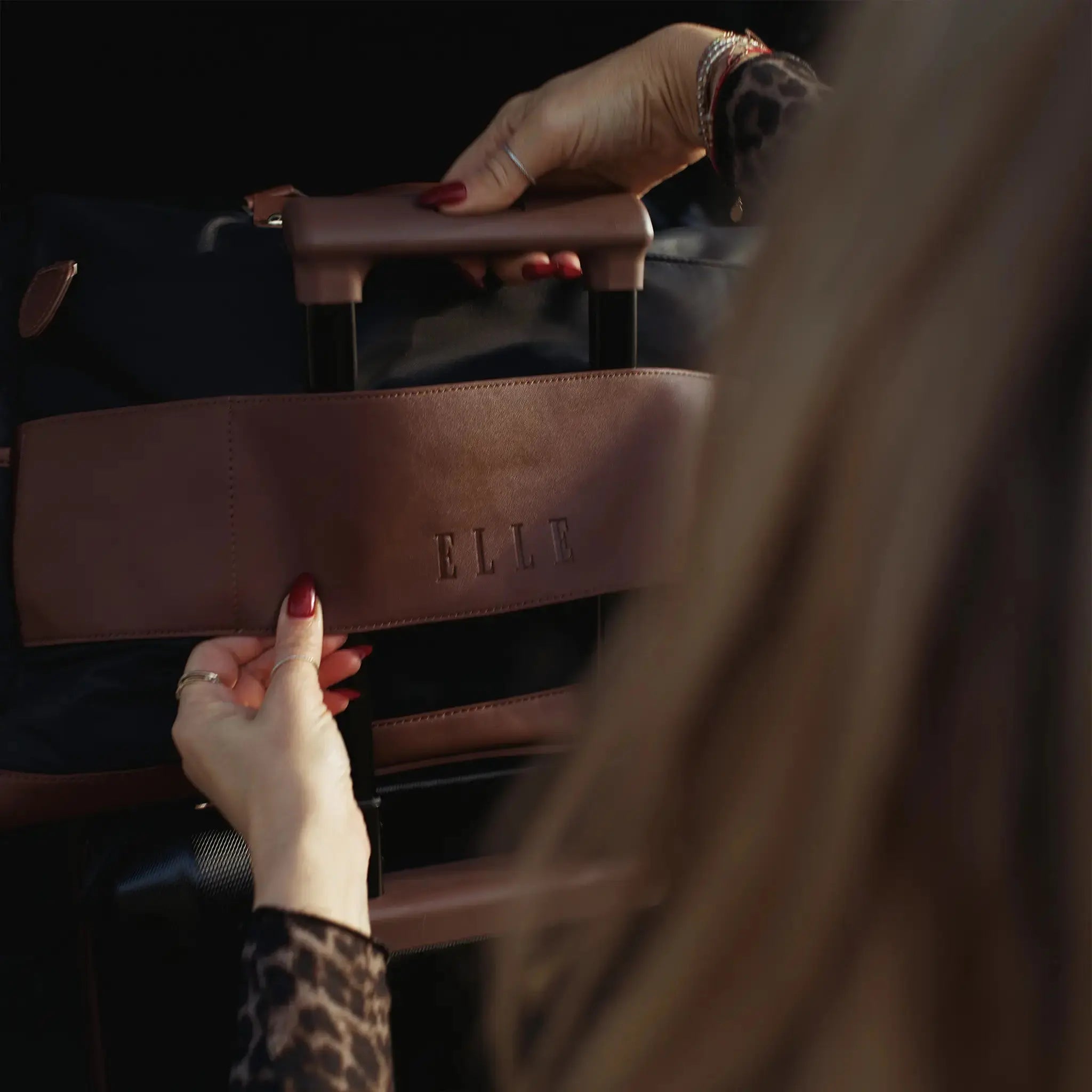 Brown leather handbag with 'ELLE' branding held by a person.