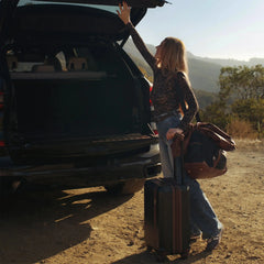 Woman with a suitcase by an open car trunk in a scenic outdoor setting