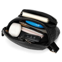 Black crossbody bag with items including a phone, pen, and remote control.