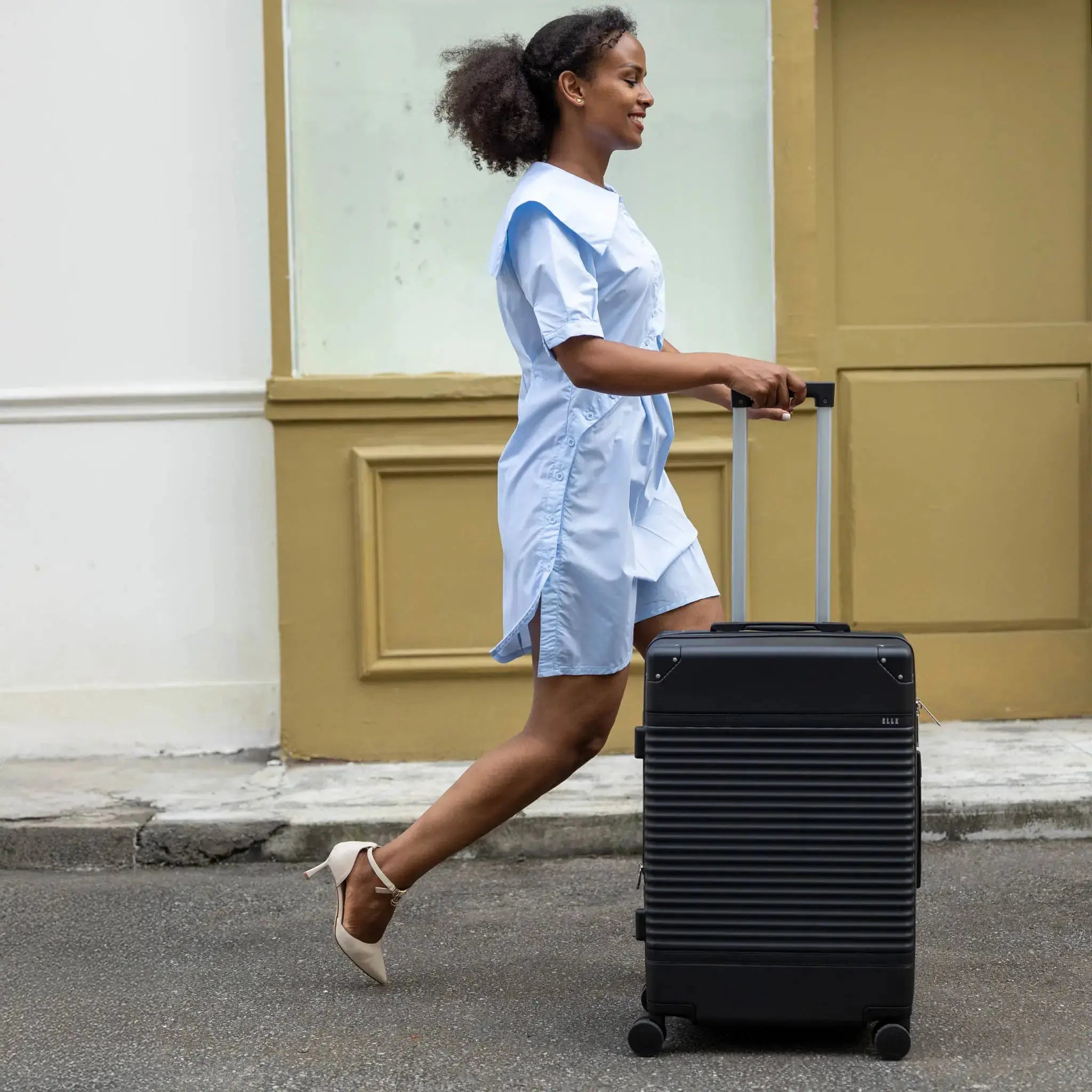 Woman pulling a black suitcase on a street