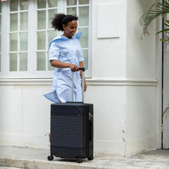 Woman in a light blue outfit pulling a black suitcase outside a building.