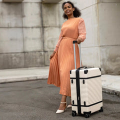 Woman in a peach dress holding a white suitcase against a stone wall.