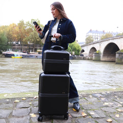 Woman with black suitcases by a river with a bridge in the background