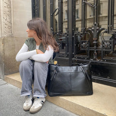 Person sitting on a step with a black leather bag next to them, in front of an ornate metal gate.