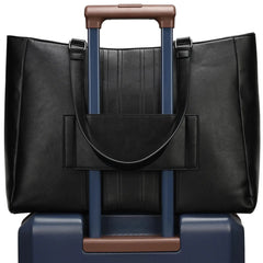 Black leather tote bag with brown handle on top of a blue suitcase with brown handle