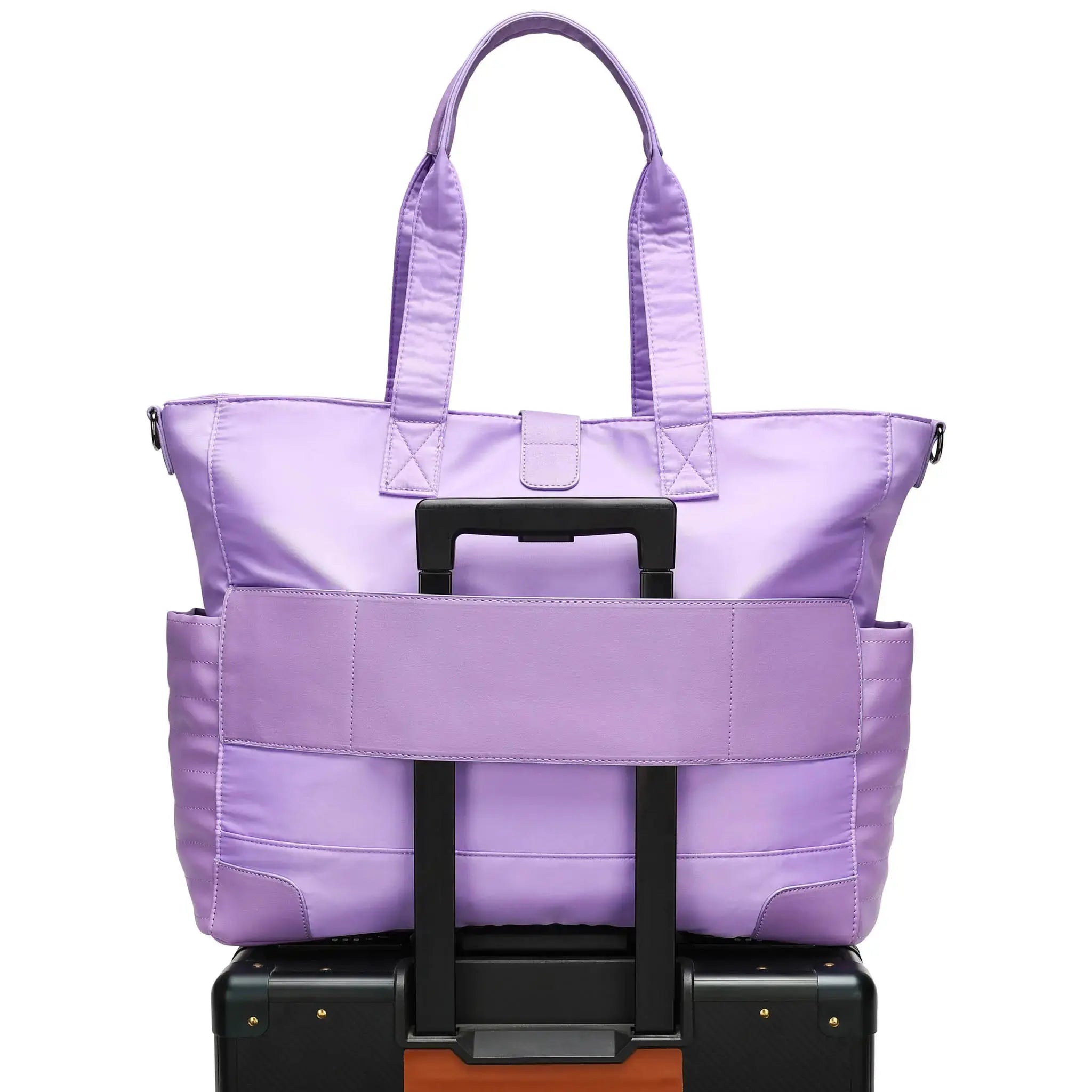 Purple tote bag stacked on top of a black suitcase with a white background