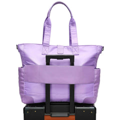 Purple tote bag stacked on top of a black suitcase with a white background