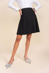 Person wearing a black pleated skirt and white top on a beige background