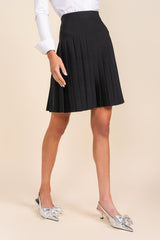 Person wearing a black pleated skirt with silver shoes on a beige background