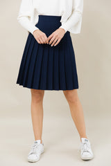 Person wearing a navy pleated skirt with a white top and white sneakers on a beige background