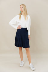 Woman wearing a white blouse and navy skirt on a beige background