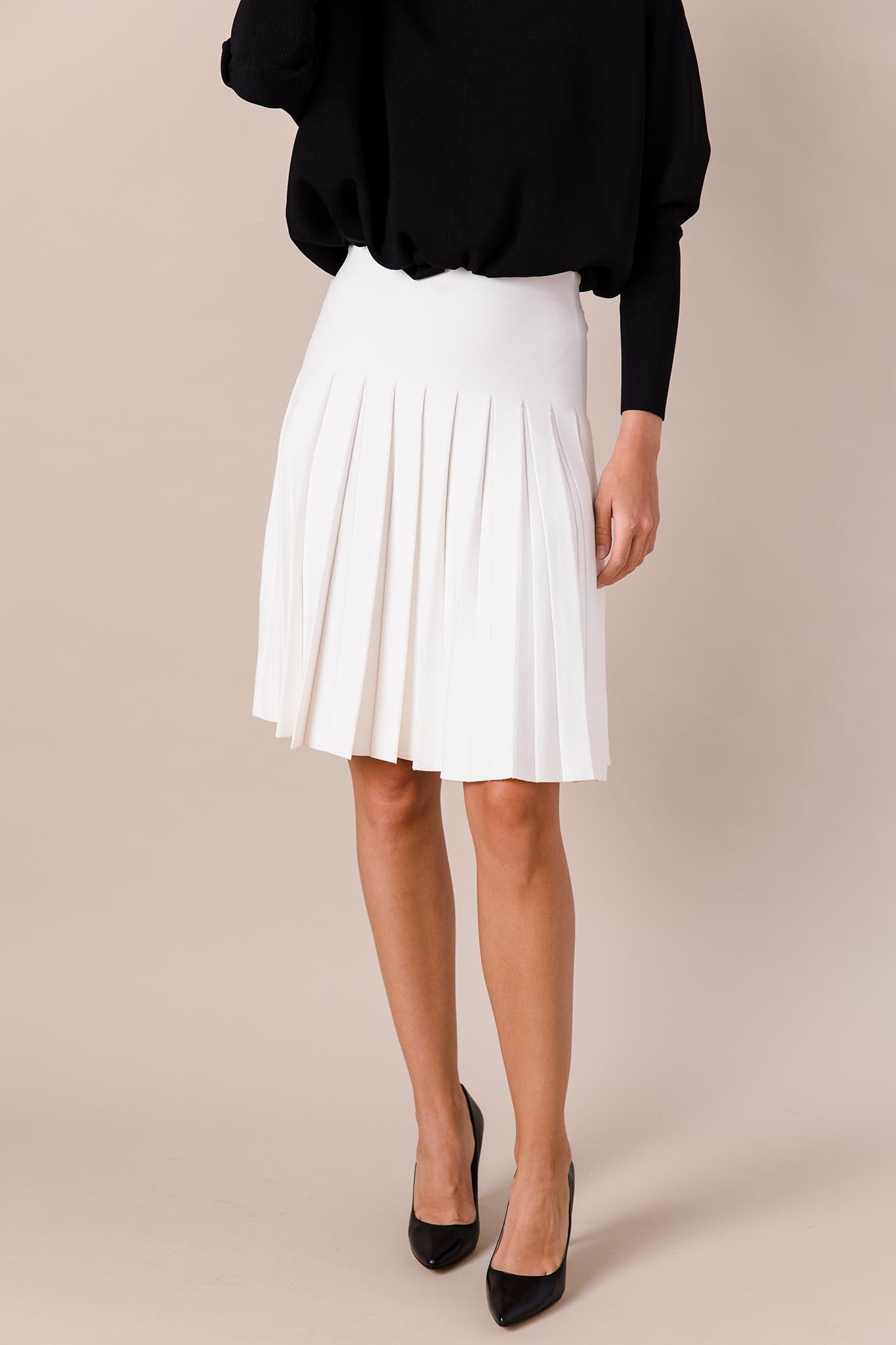 Person wearing a black top and white pleated skirt on a beige background